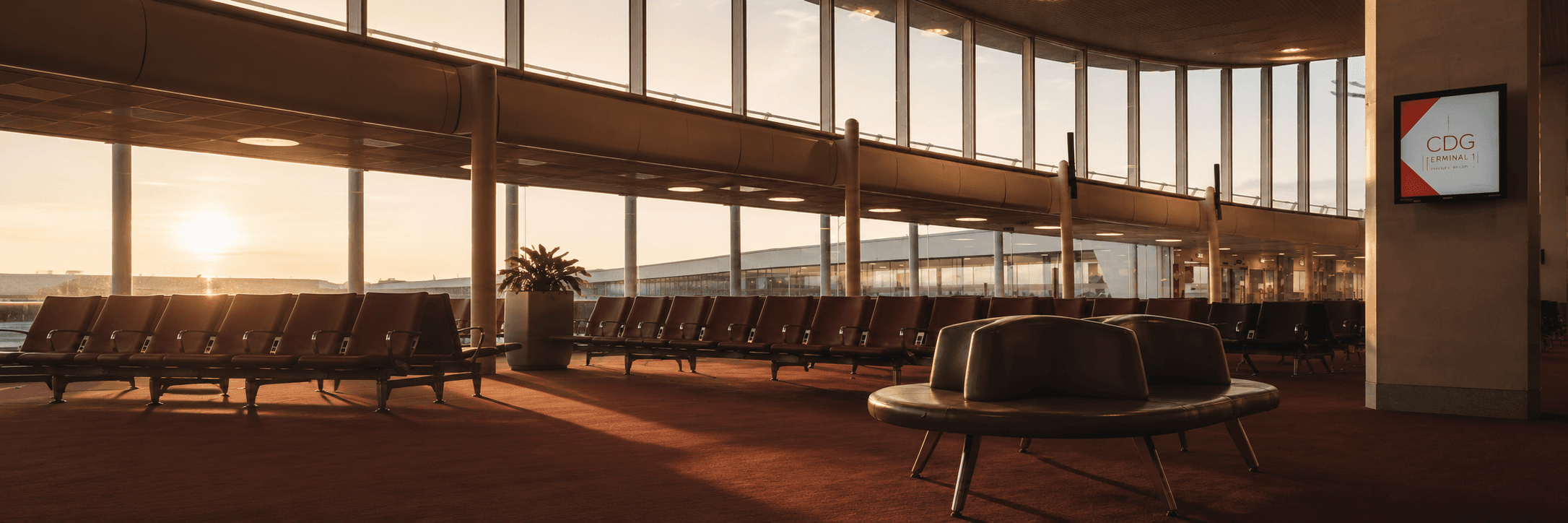 Salle d'embarquement du Terminal 1 de Roissy au soleil couchant, rangées de sièges vides sous la verrière courbe.